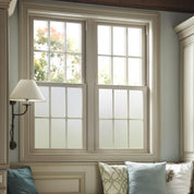 Window with frosted window vinyl on the lower half, decorative white frame and light blue pillows on a sofa.