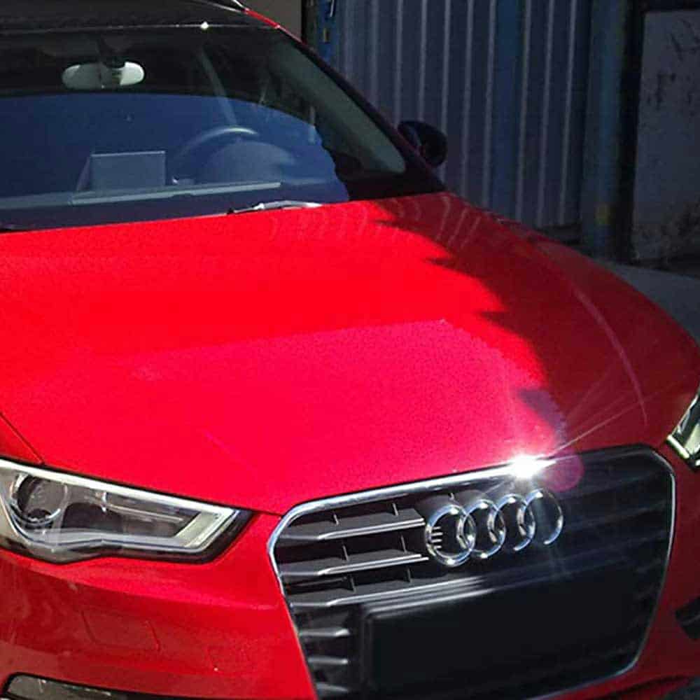 Close-up of an Oracol Gloss Cardinal Red car's front grille with headlights on.