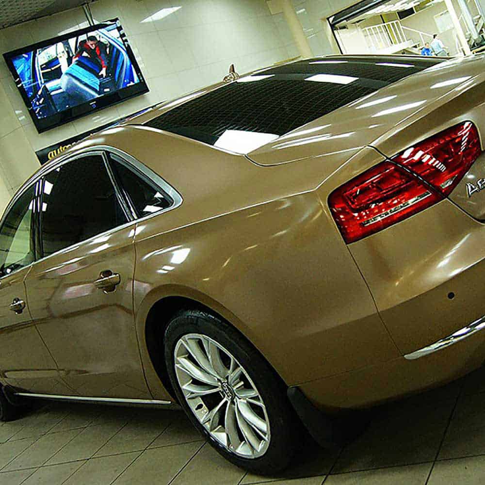 Oracal Gloss Brass Metallic car in a showroom with a television screen displaying car content