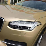 Close-up of an Oracal Gloss Brass Metallic car's headlight with a visible brand logo on the hood
