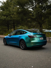 Oracal Gloss Aquamarine installed on a Tesla car parked on a road with trees