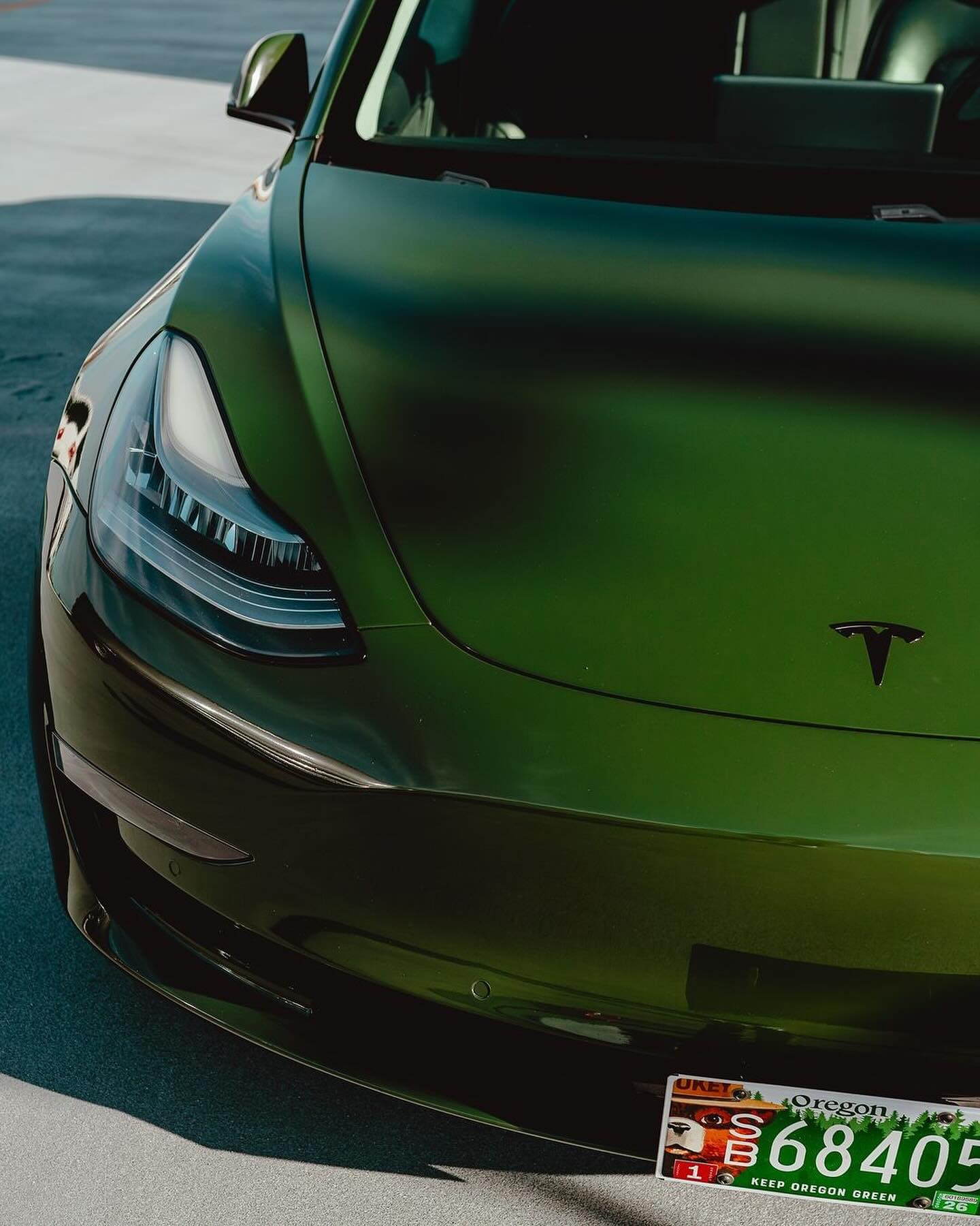 Close-up of a Oracal Gloss Bottle Green Tesla car on a road