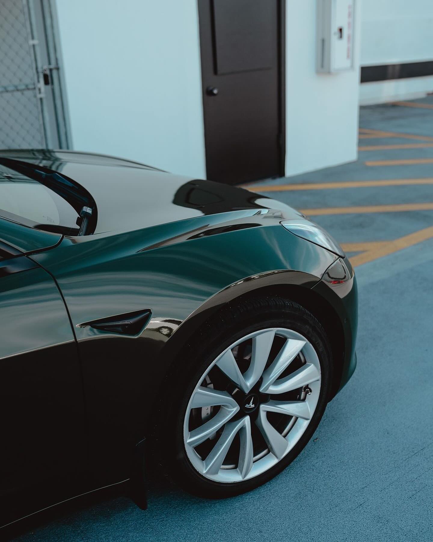 Close-up of an Oracal Gloss Bottle Green car wheel on a parking lot of a building 