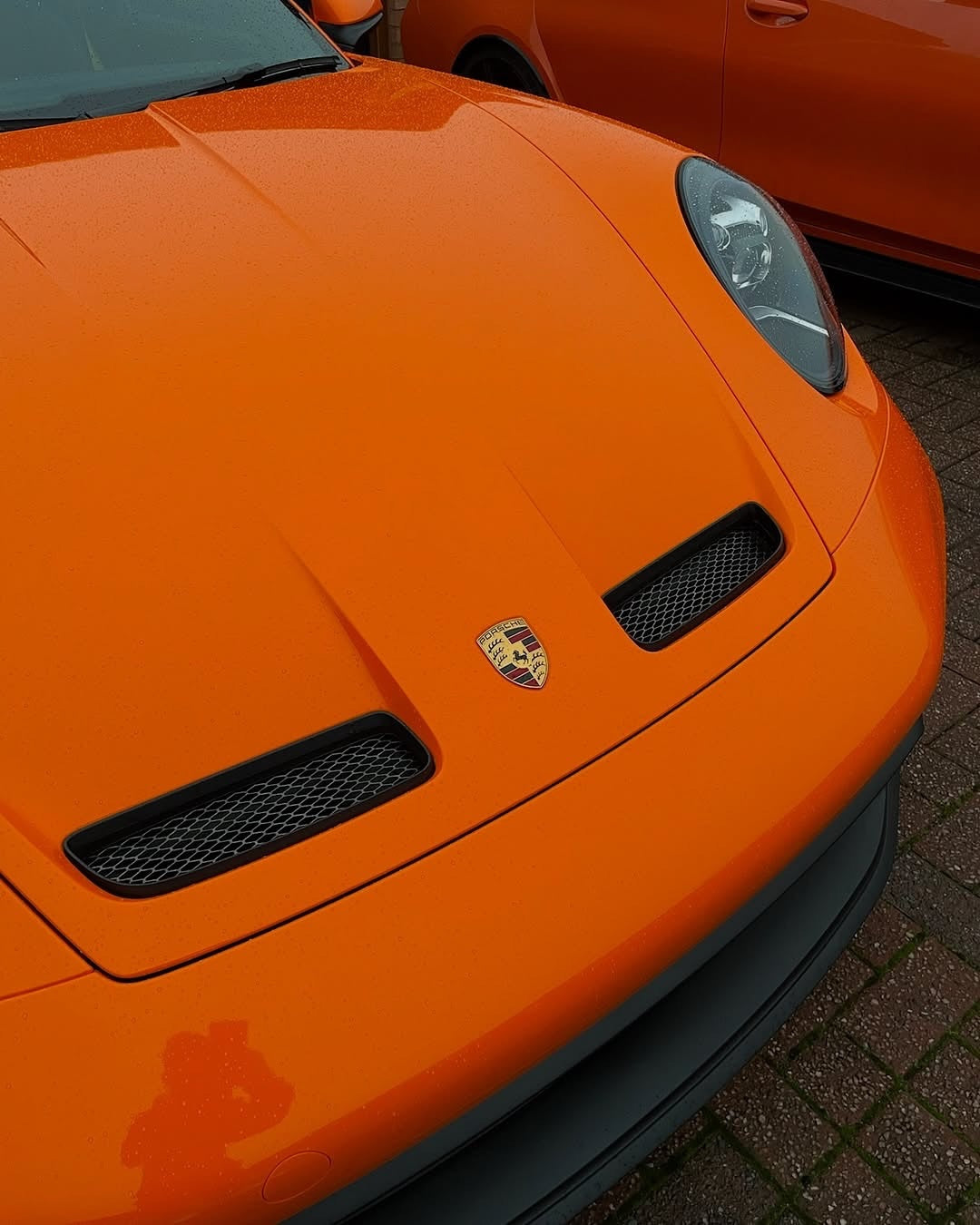 Close-up of an Oracal Gloss Daggi Orange sports car with a visible logo on a brick surface