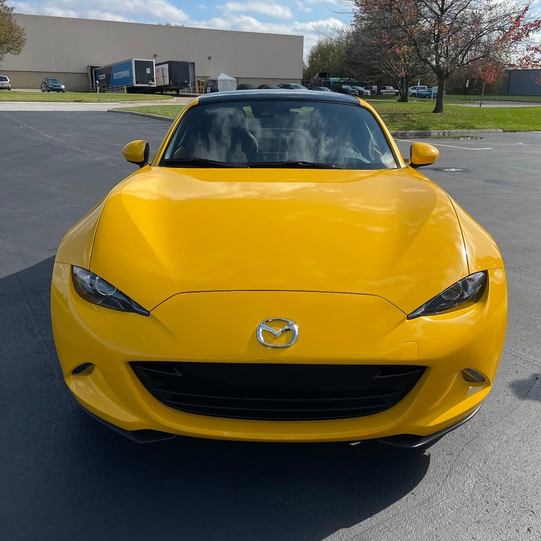 Front view of Oracal Gloss Golden Yellow installed on a Mazda car parked in a lot with a building and trees