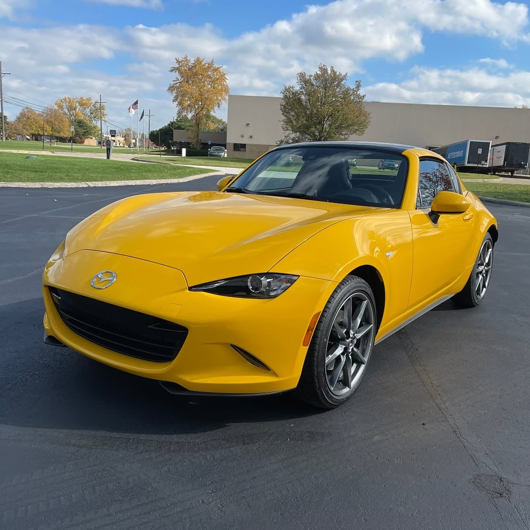 Oracal Gloss Golden Yellow installed on a Mazda car parked on a paved surface with a building and trees