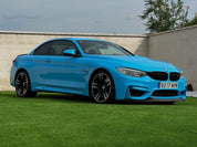Oracal Gloss Ice Blue installed on a BMW car parked on grass with a concrete wall and trees