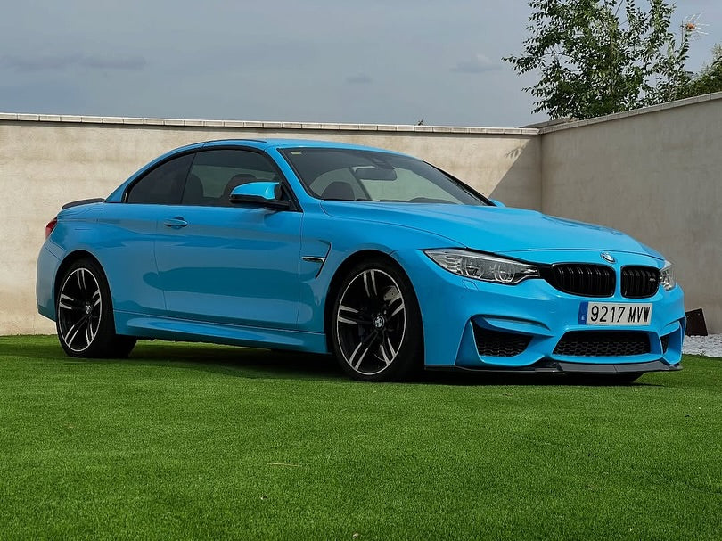 Oracal Gloss Ice Blue installed on a BMW car parked on grass with a concrete wall and trees