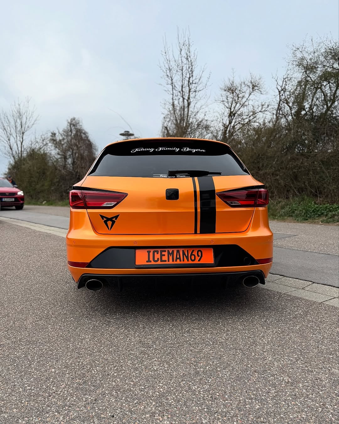 Rear close-up view of a car with Oracal Gloss Mandarin Metallic installed on a road with trees 
