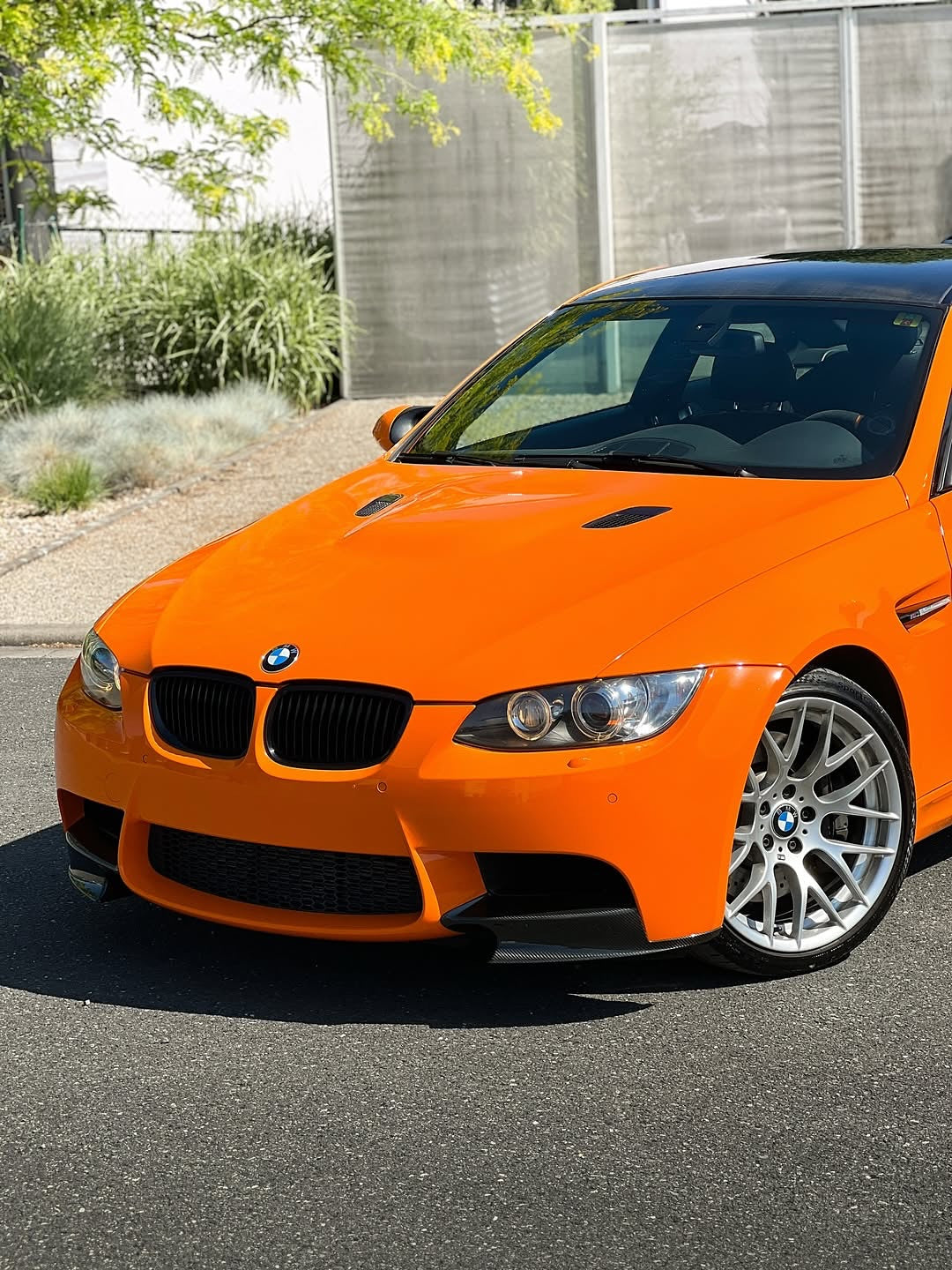 Front of Oracal Gloss Municipal Orange on a BMW car parked on a street with a building and greenery