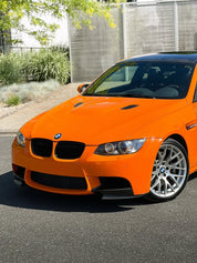 Front of Oracal Gloss Municipal Orange on a BMW car parked on a street with a building and greenery