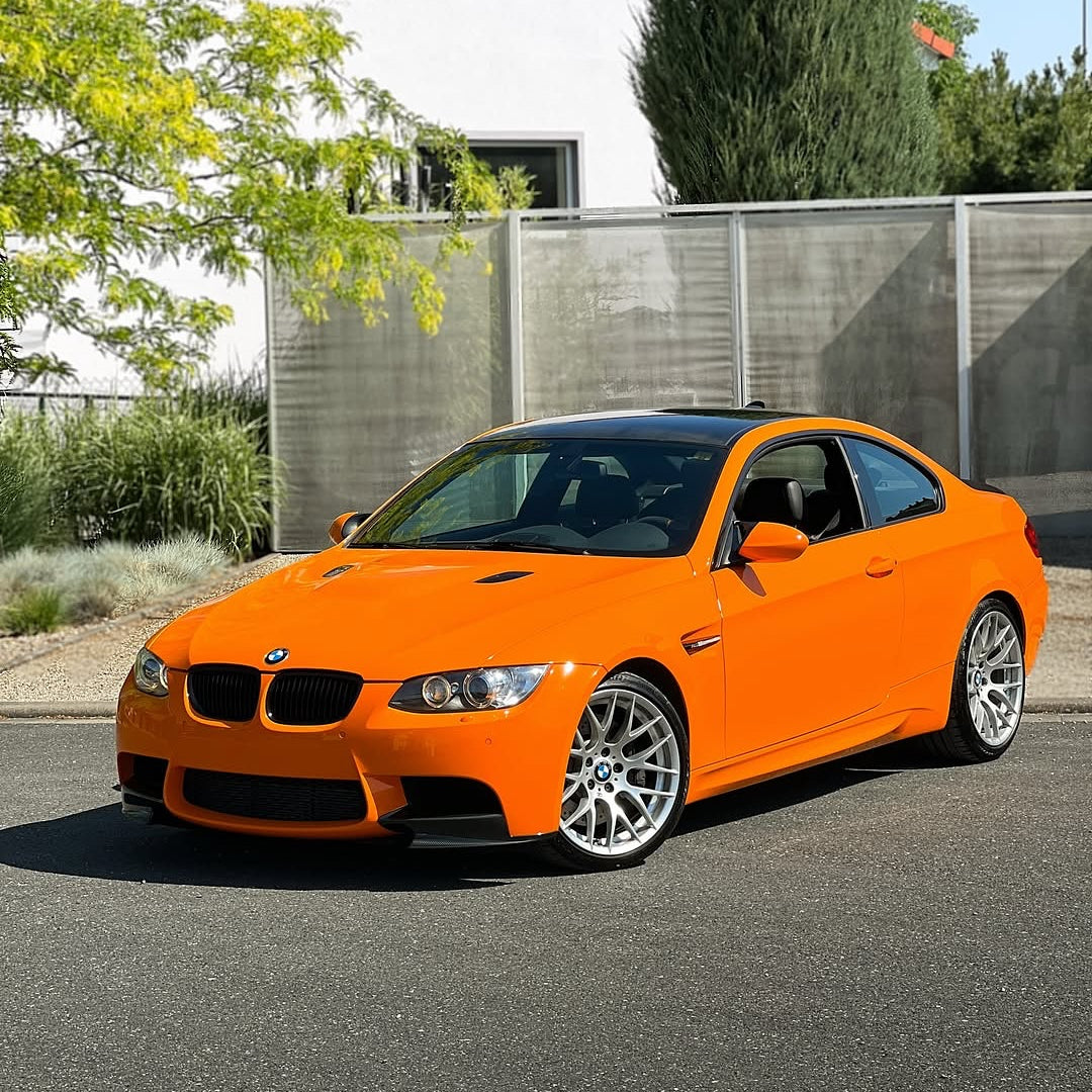 Oracal Gloss Municipal Orange on a BMW car parked on a street with a white building and trees