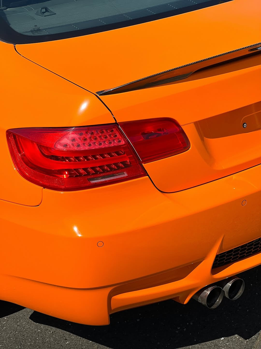 Close-up of an Oracal Gloss Municipal Orange car's rear end with a focus on the taillight and exhaust