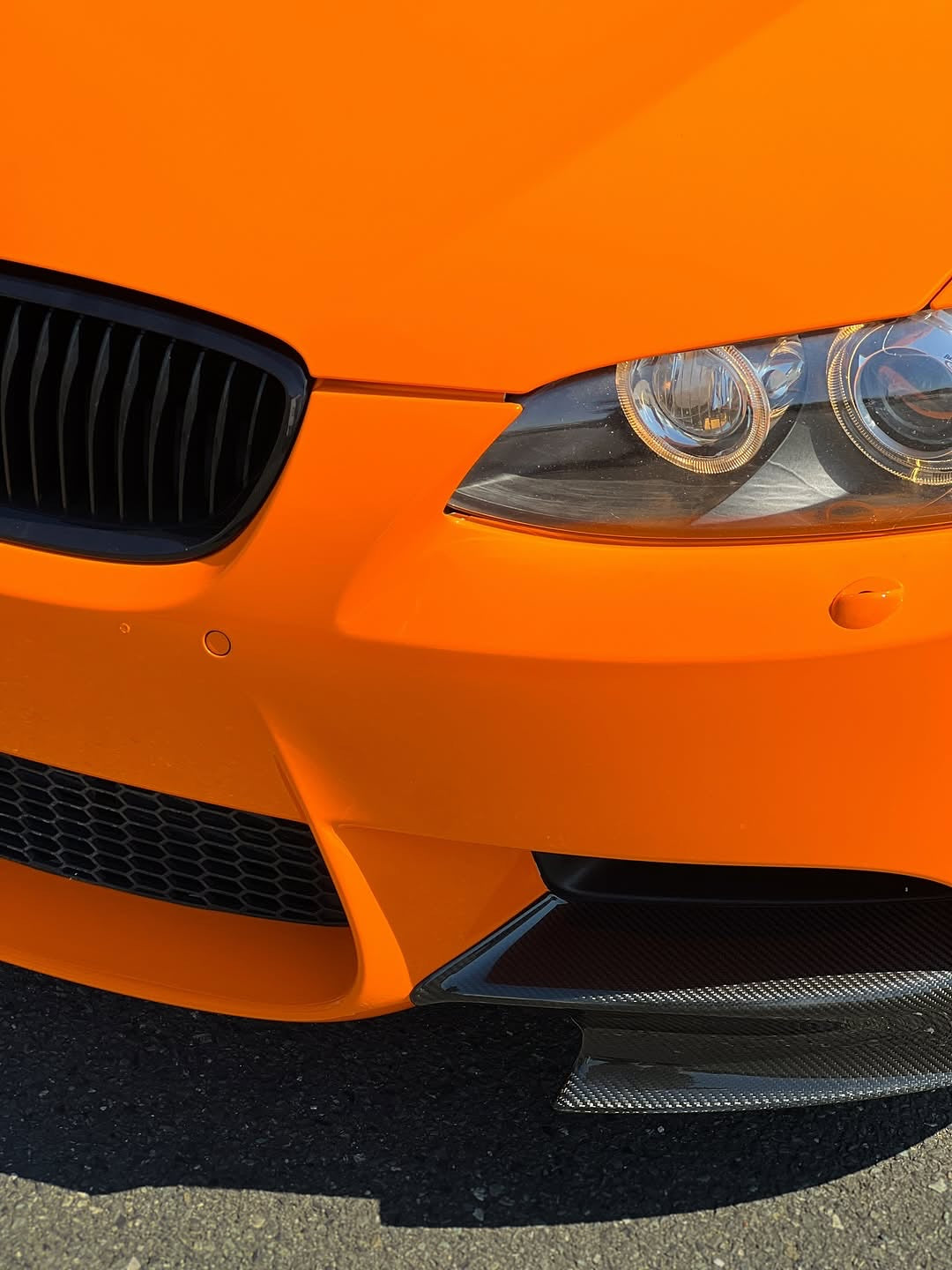 Close-up of an Oracal Gloss Municipal Orange car's front bumper and headlight
