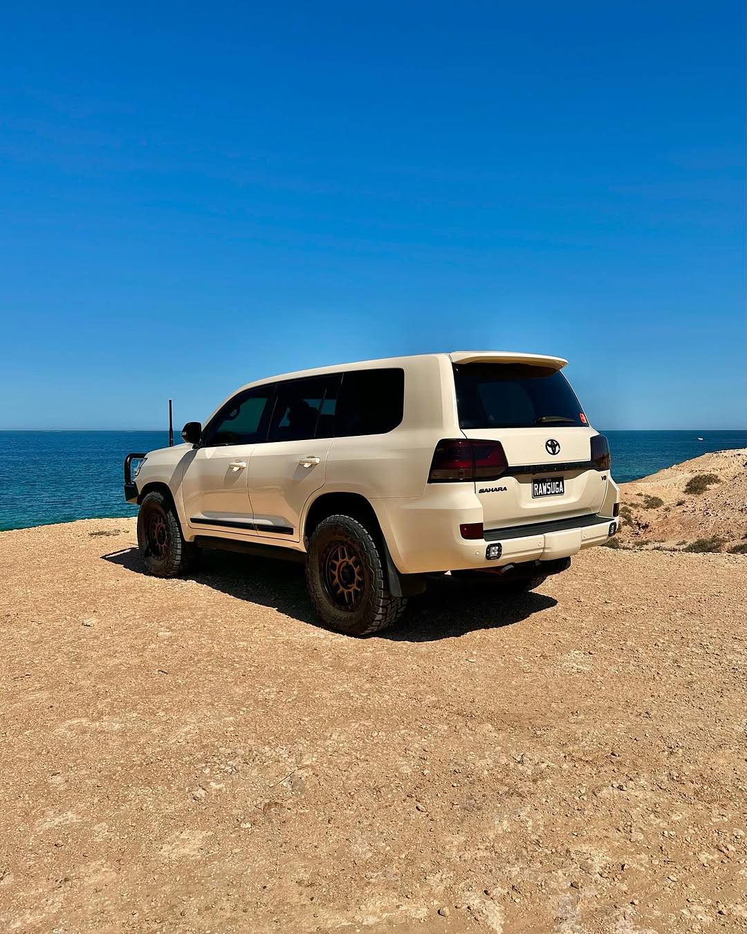 Oracal Gloss Papyrus SUV parked on a rocky coastal area with clear blue sky and ocean