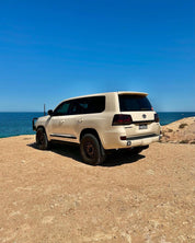 Oracal Gloss Papyrus SUV parked on a rocky coastal area with clear blue sky and ocean