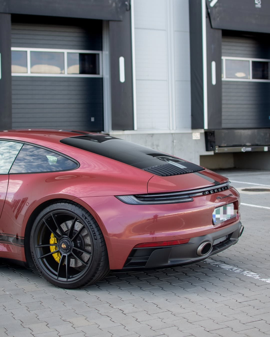 Oracal Gloss Red Brown Metallic installed on a Porsche car parked in front of a building with garage doors