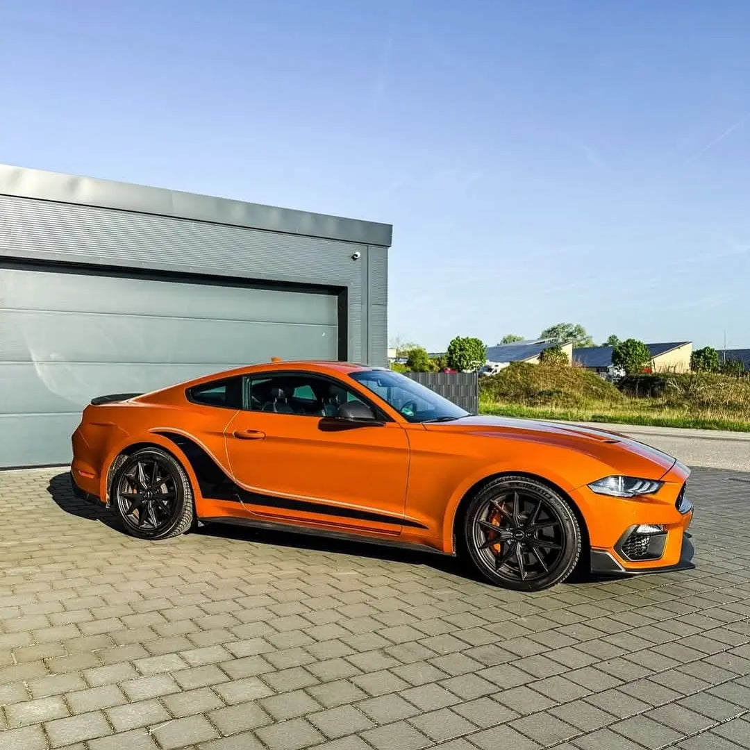 Oracal Gloss Tangerine Dream sports car parked on a paved area with a building and greenery