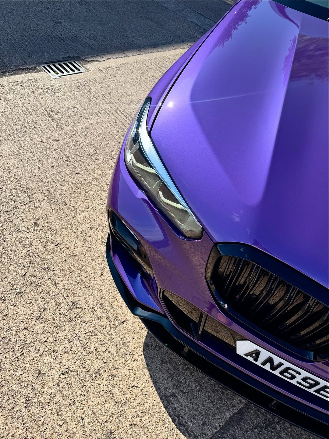 Close-up of an Oracal Gloss Violet Metallic wrap on a car's front grille and headlight on a pavement