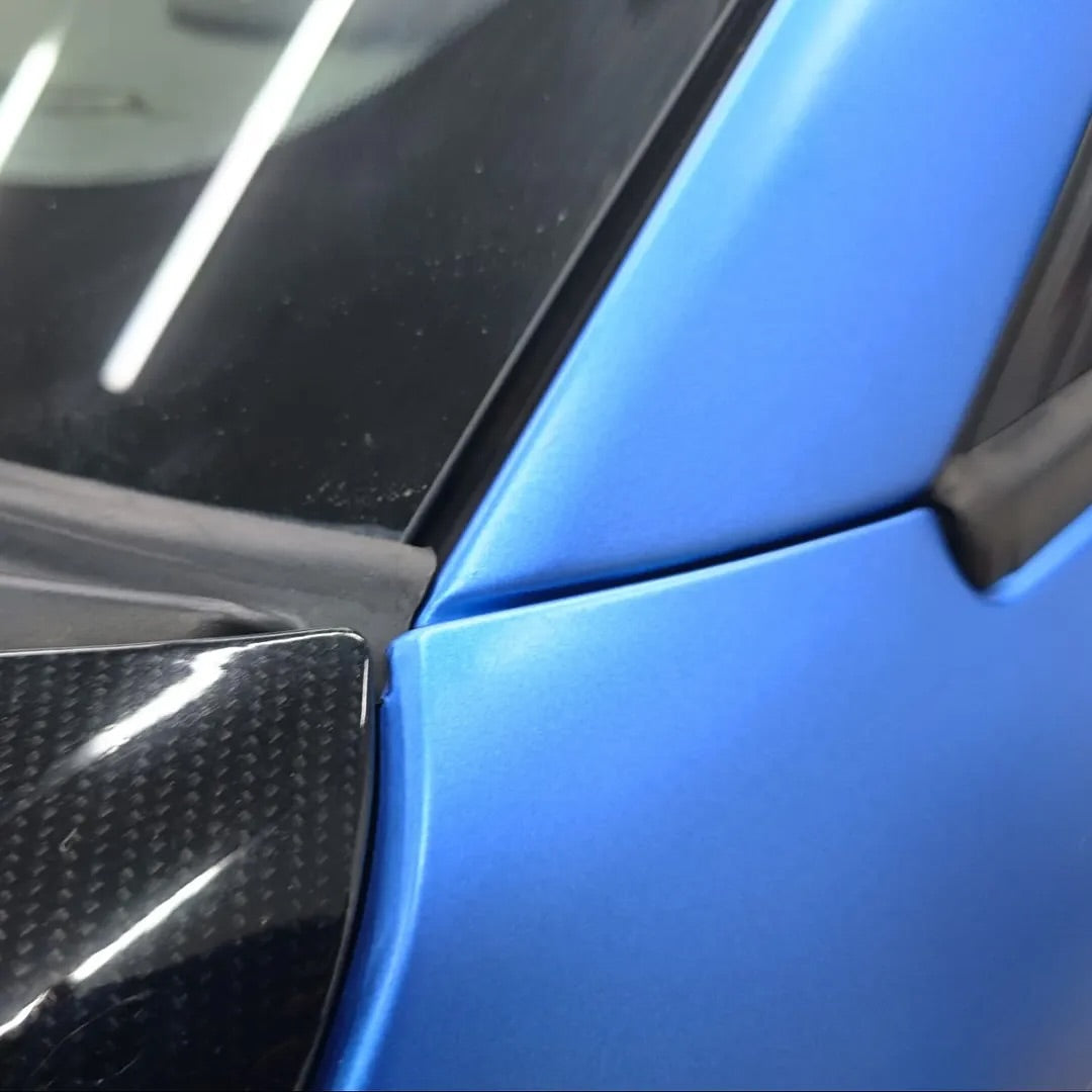 Close-up of an Oracal Matte Azure Blue Metallic car's side panel with carbon fiber texture