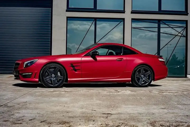 Oracal Matte Dark Red Metallic sports car parked in front of a modern building with large windows