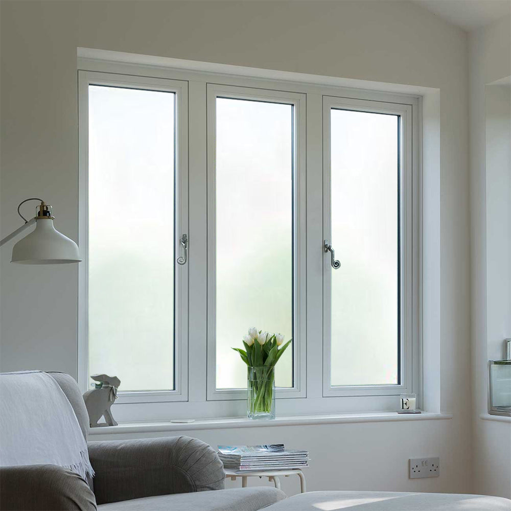 White frosted window film covering three full window panes in a living room, with a sofa and reading lamp nearby.