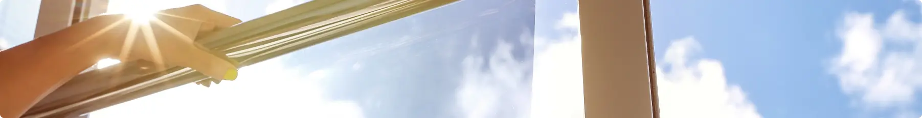 Heat reflective window film being held up to a window with the sun in the background