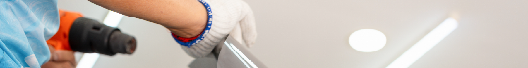 A person holding a heat gun with a glove is installing vinyl with installation aids