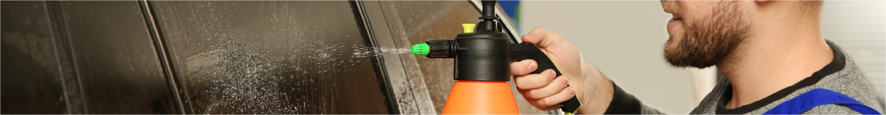 A fitter using a window tint sprayer on a window
